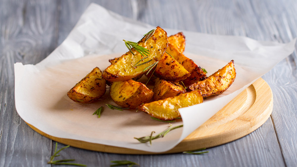 Kartoffel Wedges mit Rosmarin liegen auf Holzbrett