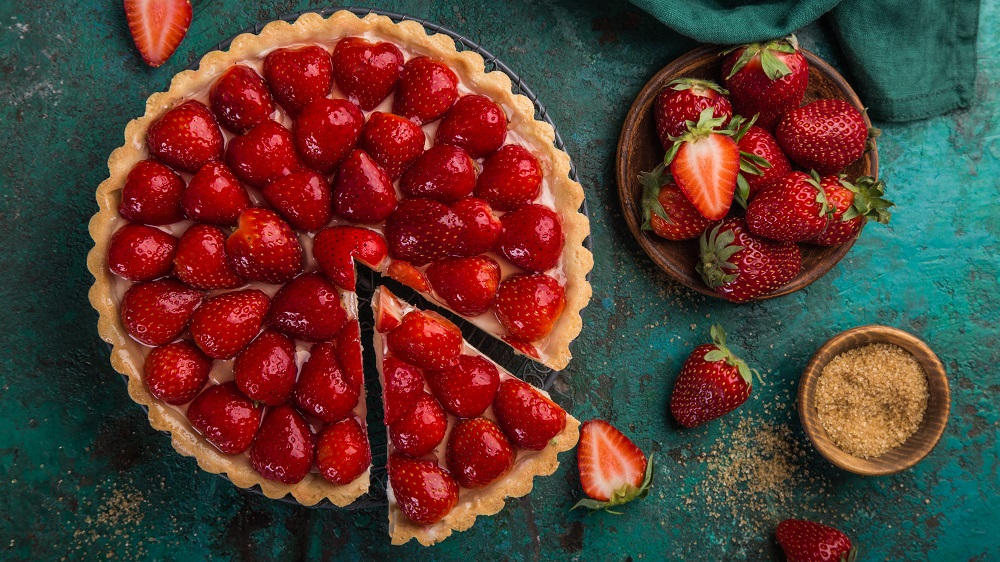 Erdbeerkuchen mit Zutaten und einem Stück, das herausgenommen wird.