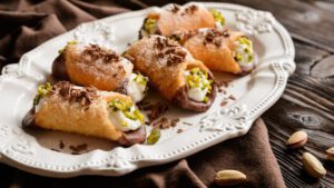 Cannoli mit Ricottacremefüllung auf einem weißen Teller mit Pistazien und Schokosplittern garniert.