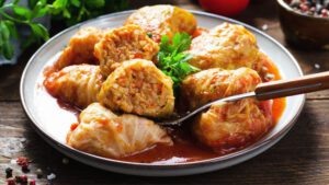 Sarma mit roter Soße und Petersilie auf einem Teller angerichtet.