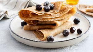 Crêpes mit Blaubeeren auf weißem Teller angerichtet.